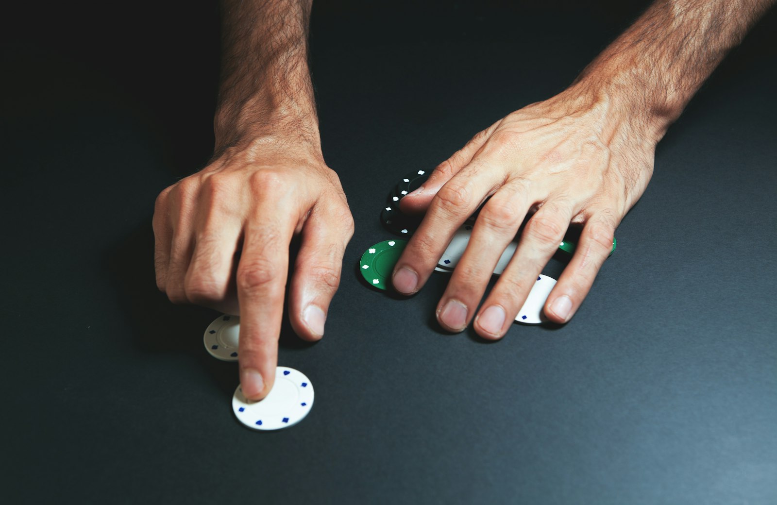Detail pokerových žetonů a rukou hráče v intimní atmosféře kasina